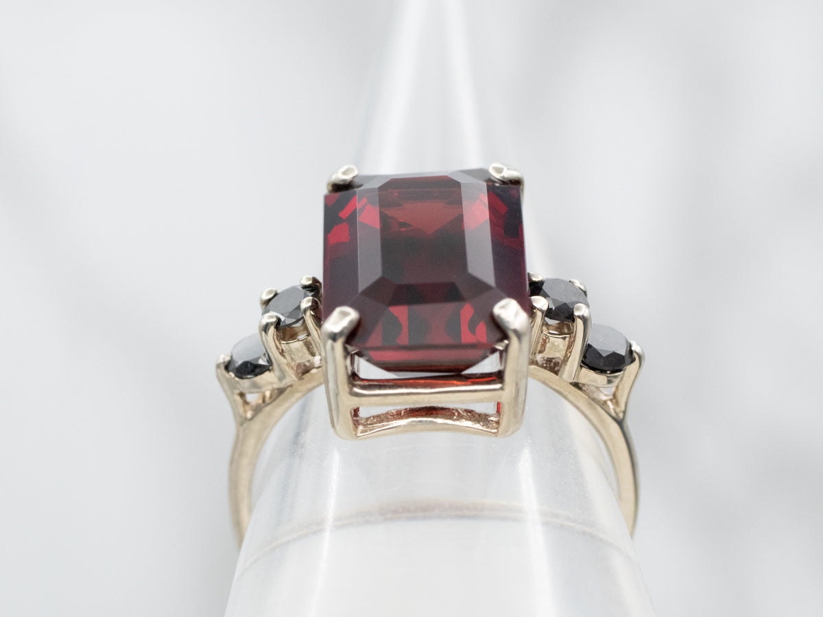 Anillo de oro blanco con granate de talla esmeralda y detalles de diamantes negros