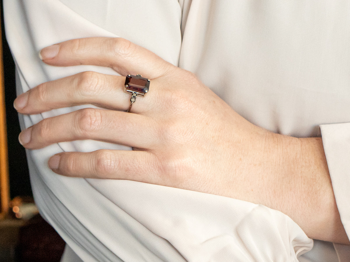 Anillo de oro blanco con granate de talla esmeralda y detalles de diamantes negros